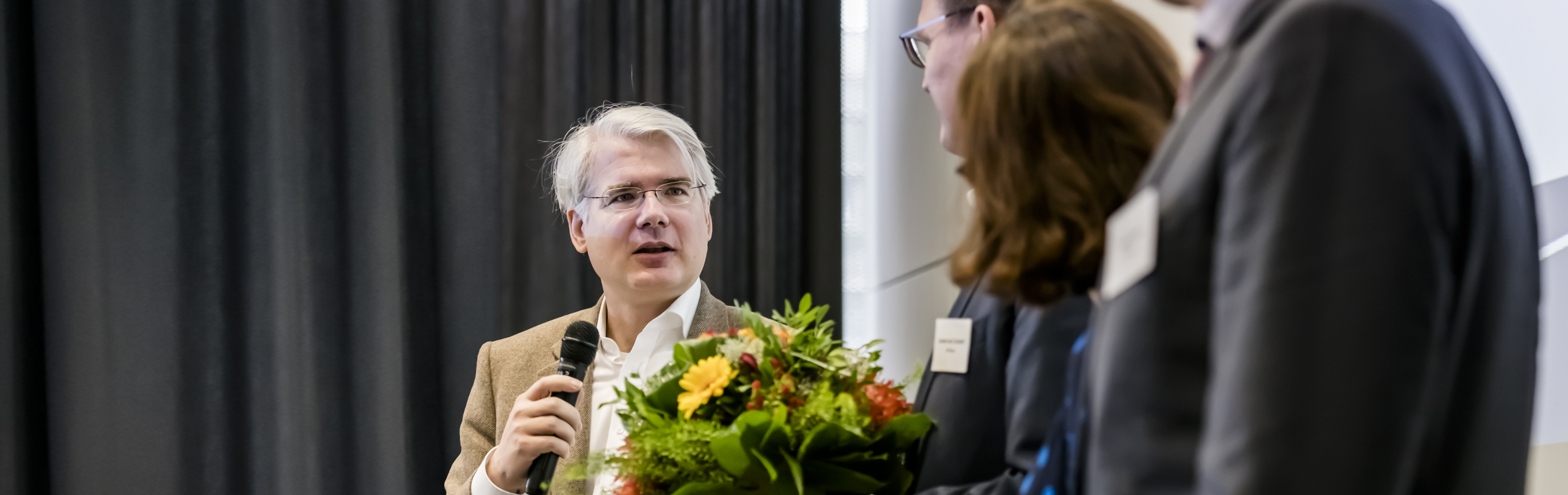 Man mit beigen Auszug, Blumen und Mikrophon auf dem Podium