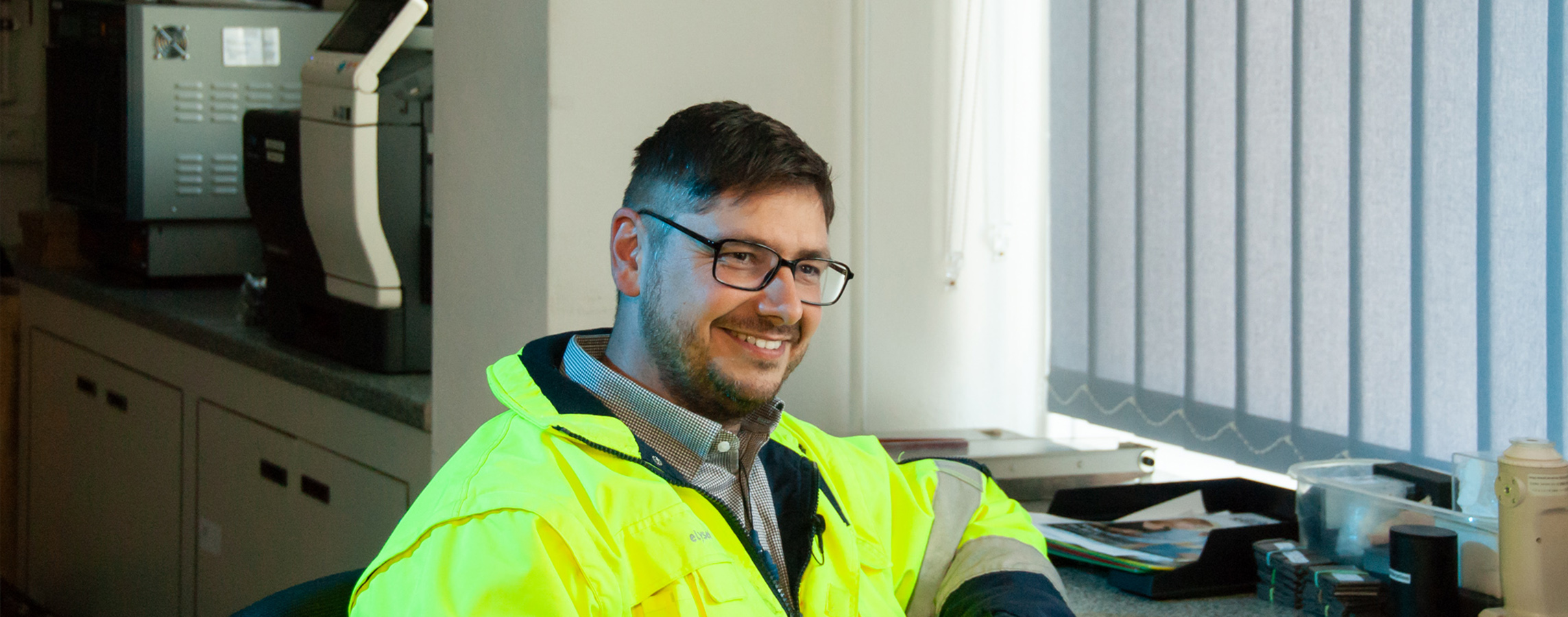 Man mit Brille in gelber Warnjacke am Schreibtisch