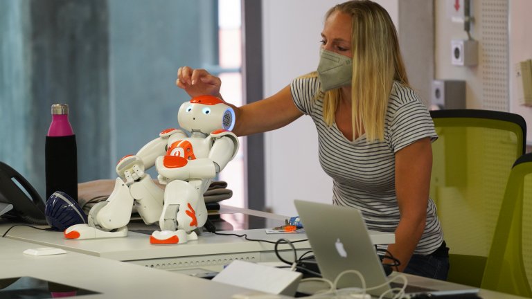 Frau berührt kleinen Roboter auf Tisch